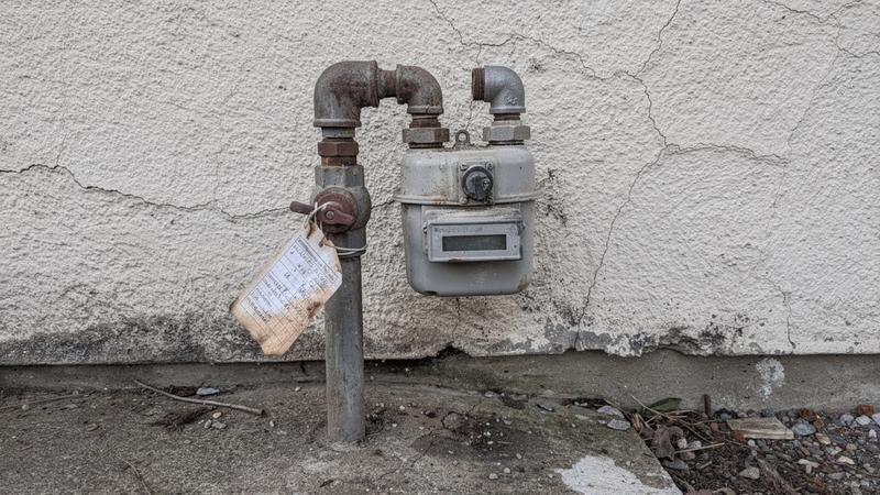 Gas inlet pipe and meter with a dated inspection tag on the wall of a village cottage in Kyiv Oblast.